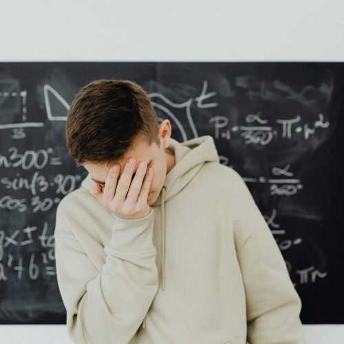 Student Mistake A young man stands in front of a blackboard, looking frustrated amidst complex calculations.